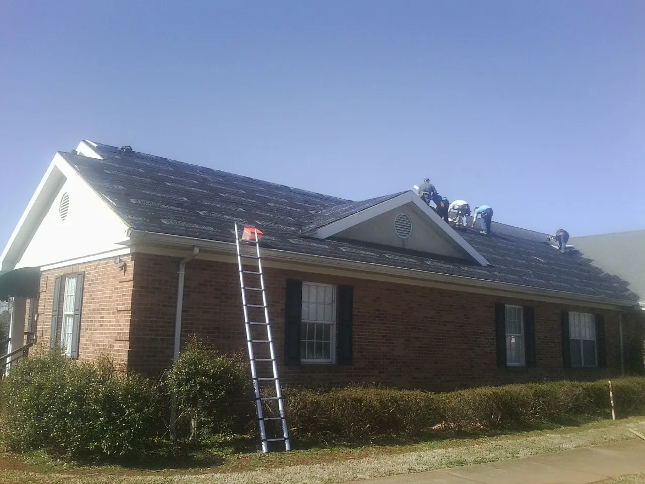 Crew tearing shingles off a brick ranch roof with a ladder set — Emergency Roof Repair work by our crew in Sharpsburg